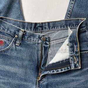 May include: A pair of blue denim jeans with a zipper fly and a button closure. The jeans are folded in half and the zipper is open.