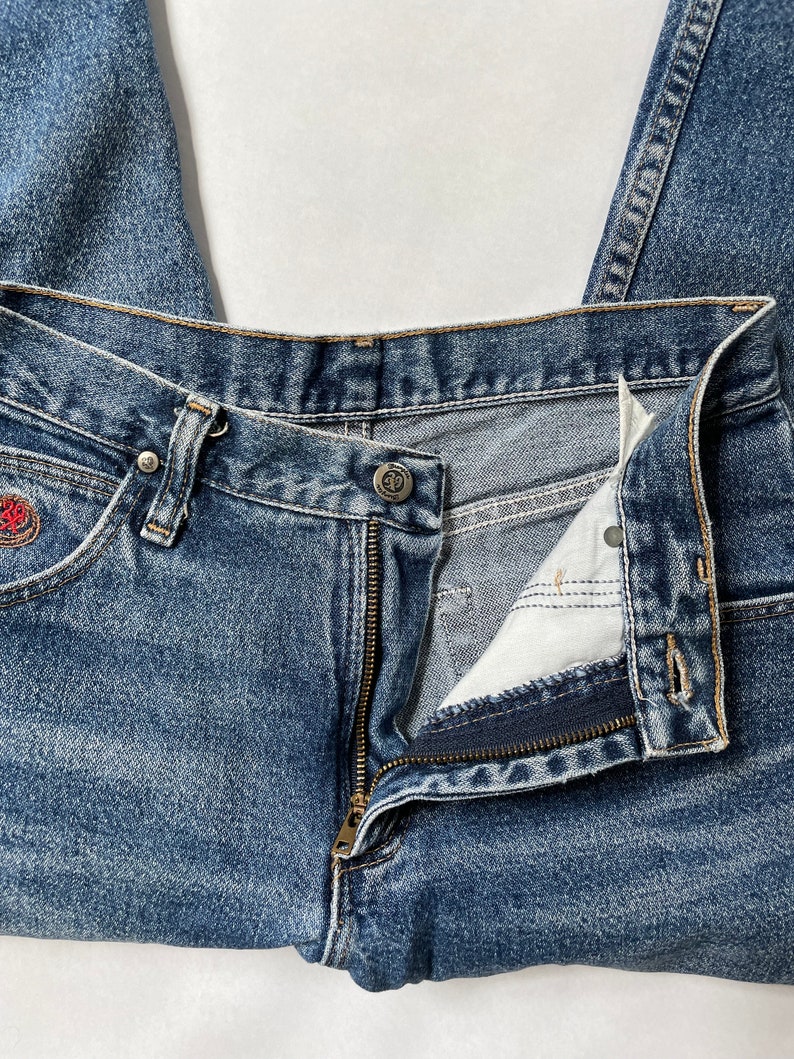 May include: A pair of blue denim jeans with a zipper fly and a button closure. The jeans are folded in half and the zipper is open.