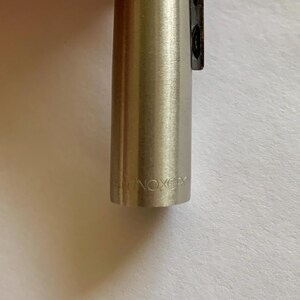 May include: Close-up of a silver-colored pen with the text "INOXCR" engraved on the barrel. The pen has a sleek, metallic finish and a black clip. The pen is likely a writing instrument.