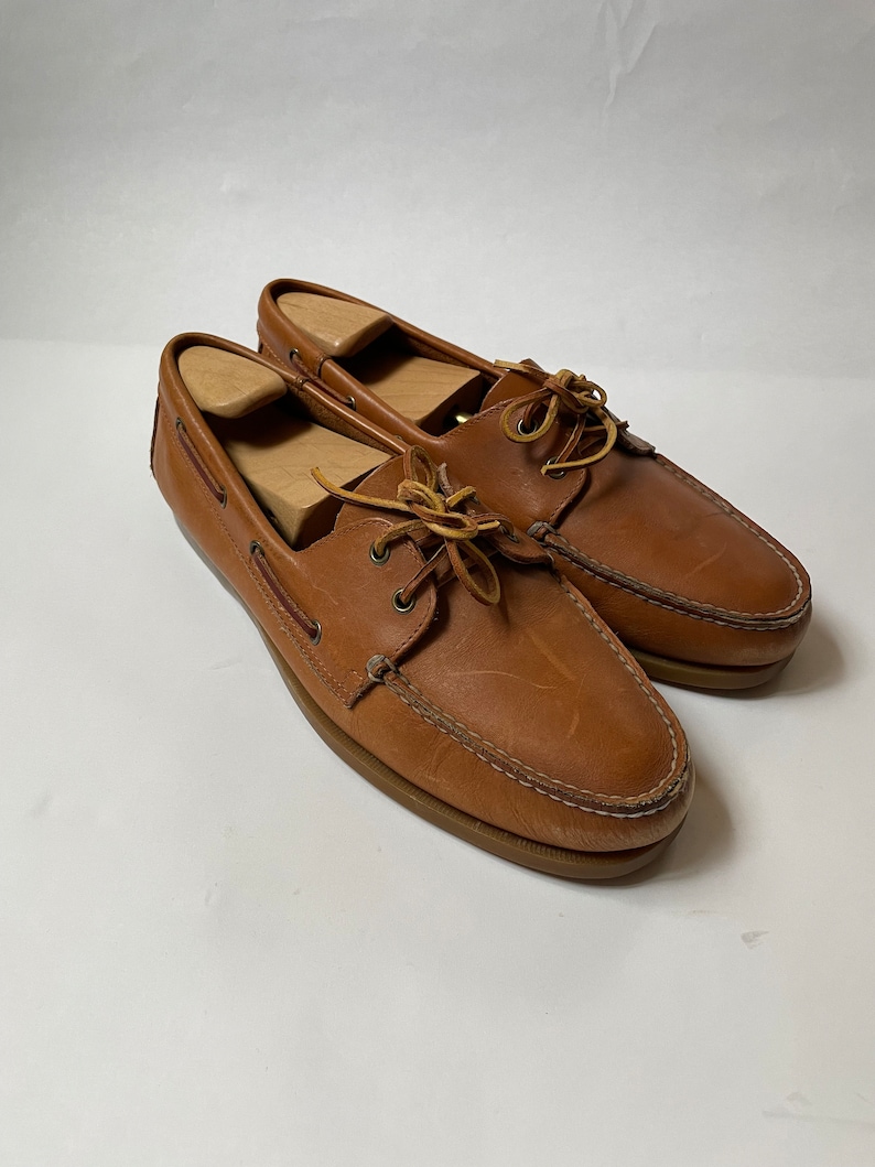 May include: A pair of brown leather boat shoes with laces. The shoes have a light brown sole and are worn.