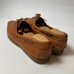 May include: A pair of brown leather boat shoes with laces. The shoes have a white stitching detail around the sole.