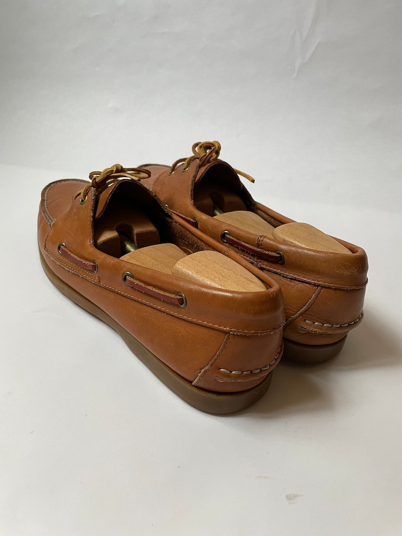 May include: A pair of brown leather boat shoes with laces. The shoes have a white stitching detail around the sole.