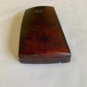 May include: A rectangular, dark brown box with a textured surface. The box has a slightly curved top and a small, decorative element near the top. The box appears to be made of a hard material.