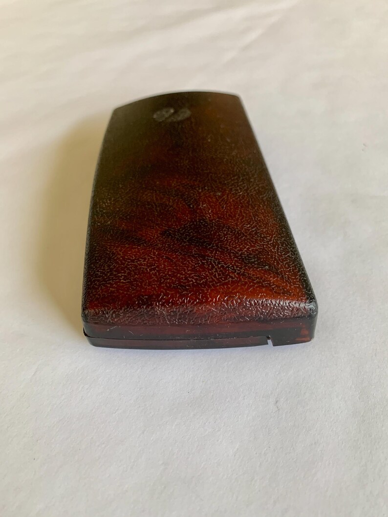 May include: A rectangular, dark brown box with a textured surface. The box has a slightly curved top and a small, decorative element near the top. The box appears to be made of a hard material.