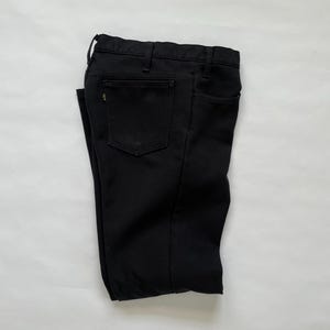 May include: A pair of folded black pants. The pants have a classic five-pocket design with a button and zipper closure. The pants are made of a solid black fabric and appear to be new.