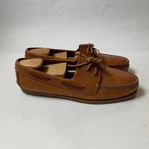 May include: A pair of brown leather boat shoes with laces. The shoes have a brown leather sole and are in good condition.