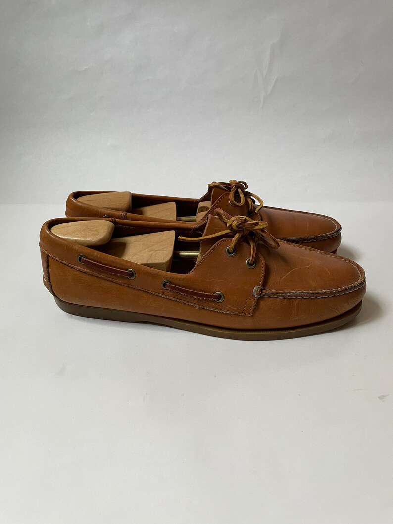 May include: A pair of brown leather boat shoes with laces. The shoes have a brown leather sole and are in good condition.