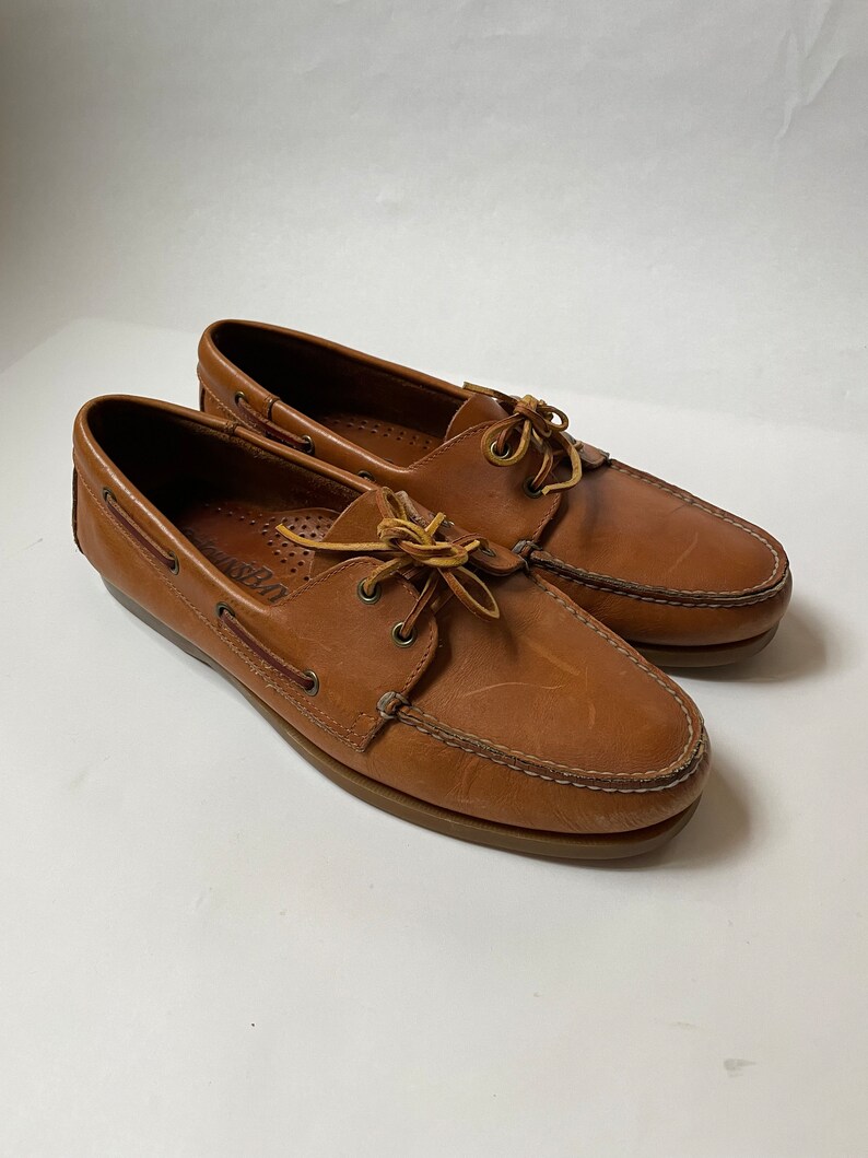 May include: A pair of brown leather boat shoes with laces. The shoes have a light brown sole and are made of a soft, supple leather.
