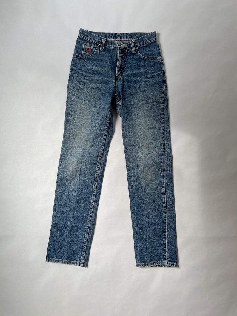 May include: A pair of blue denim jeans with a button fly and a red logo on the back pocket.