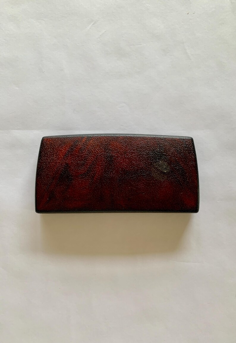 May include: A rectangular, dark red box with a textured surface. The box has rounded edges and a black border. The overall appearance suggests a vintage or antique item, possibly a case or container.