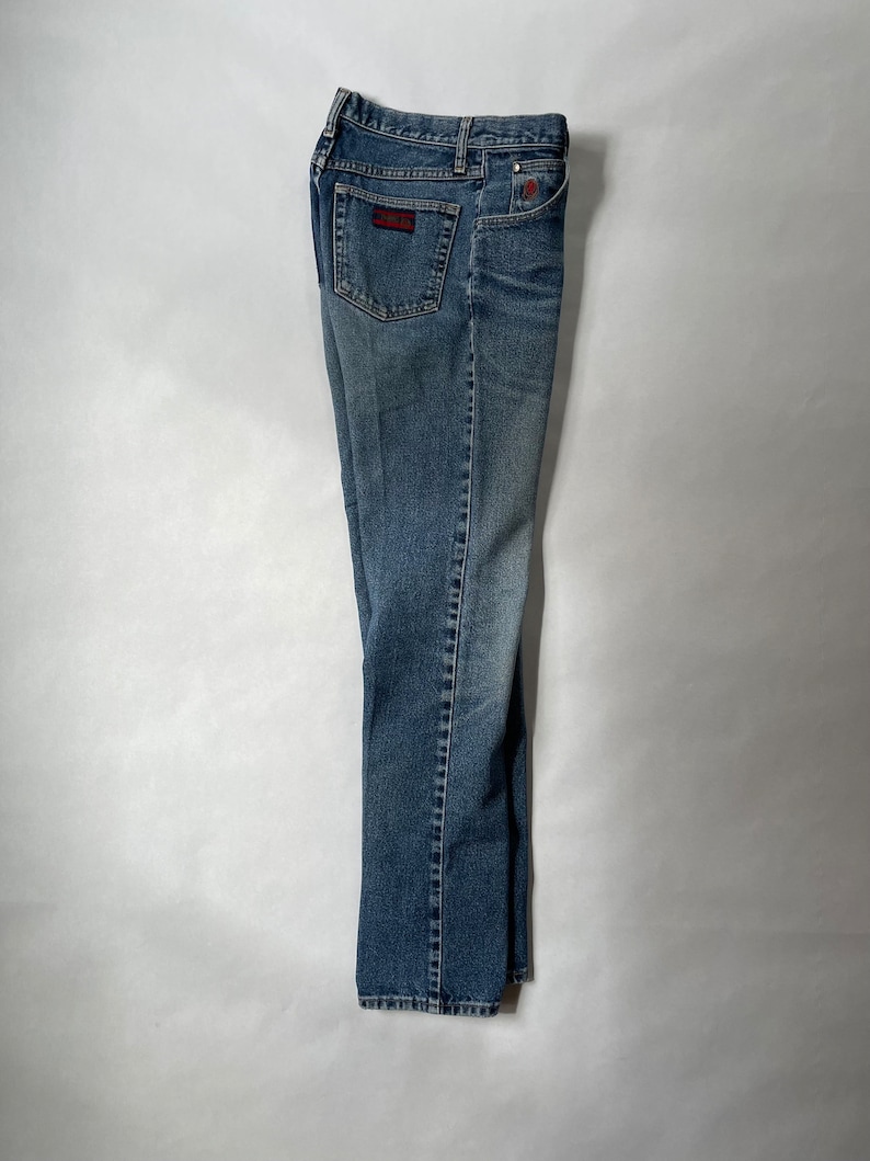May include: A pair of blue denim jeans with a red and black patch on the back pocket.