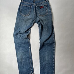 May include: A pair of blue denim jeans with a red and white patch on the back pocket.