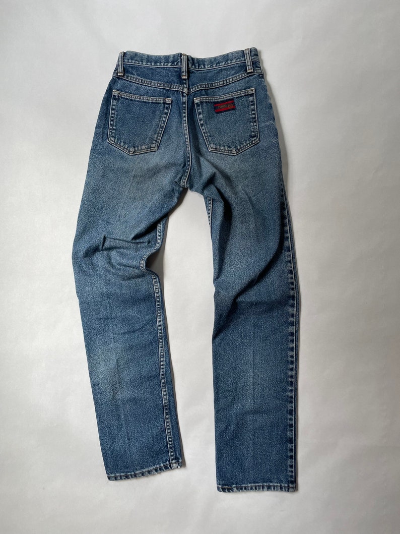 May include: A pair of blue denim jeans with a red and white patch on the back pocket.