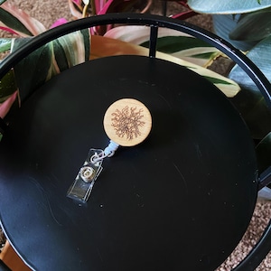 Może przedstawiać: Drewniany zwijacz do odznak z czarno-białym wzorem drzewa. Zwijacz jest przymocowany do czarno-białego sznurka.