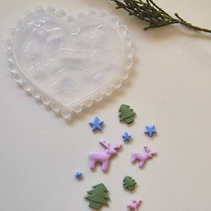 May include: A clear plastic heart-shaped mould with a raised design of Christmas trees, stars, and reindeer.  There are several small, colourful decorations made of fondant, including green trees, blue stars, and pink reindeer.