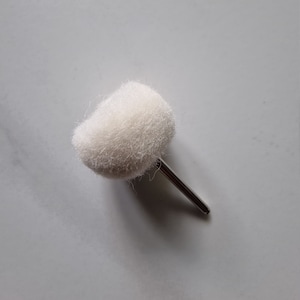 May include: A white, fluffy buffing wheel attached to a silver metal shaft. The buffing wheel is used for polishing and smoothing surfaces.