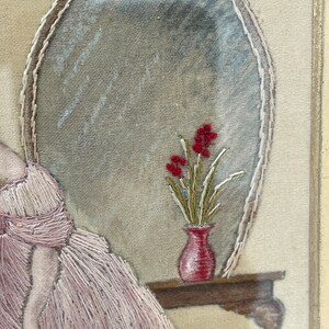 Puede incluir: Obra de arte bordada que representa a una mujer con un vestido rosa sentada junto a una mesa con un jarr&oacute;n de flores rojas. La obra est&aacute; enmarcada y tiene un aspecto vintage.
