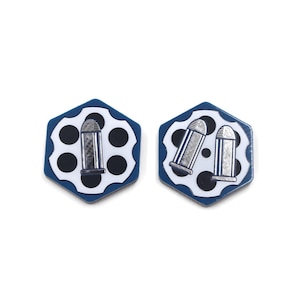 Puede incluir: Dos pendientes hexagonales con borde azul e interior blanco. Cada pendiente presenta un diseño de cilindro de revólver con detalles de bala plateada. Los pendientes están sobre un fondo blanco.