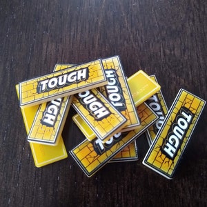 May include: A pile of yellow game tiles with the word "TOUGH" printed in black letters. The tiles have a brick pattern.