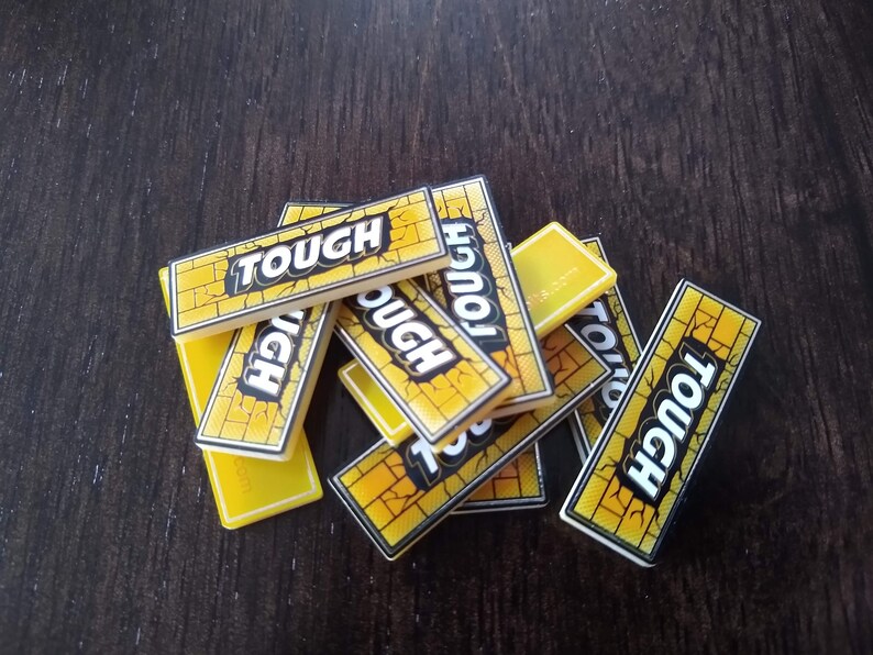 May include: A pile of yellow game tiles with the word "TOUGH" printed in black letters. The tiles have a brick pattern.