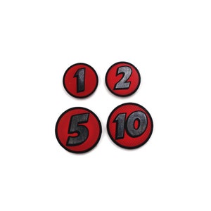 May include: Four red circular game pieces with black outlines and silver numbers. The numbers are 1, 2, 5, and 10.