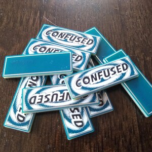May include: A stack of teal blue game tiles with white borders and black text that reads "CONFUSED".