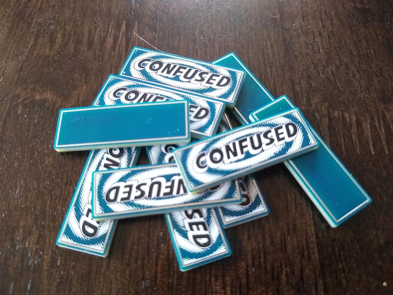 May include: A stack of teal blue game tiles with white borders and black text that reads "CONFUSED".