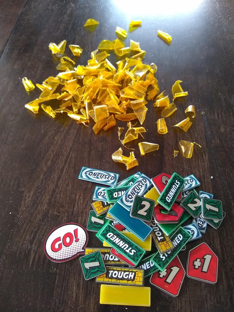 May include: A collection of colourful game pieces for a board game. The pieces are made of plastic and have various shapes and designs. Some of the pieces have numbers on them, while others have words like "Go!" and "Confused".