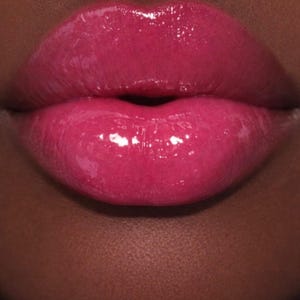 May include: Close-up of a person's lips, showcasing a vibrant, glossy fuchsia lipstick. The lips are full and well-defined, with a high-shine finish that reflects light. The skin surrounding the lips is a deep brown tone, providing a striking contrast.