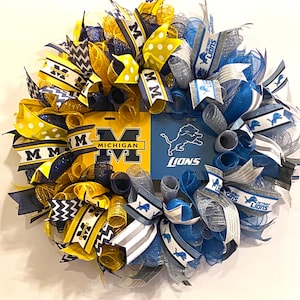 May include: A wreath decorated with blue, yellow, and silver mesh ribbon, featuring a Michigan Wolverines logo and a Detroit Lions logo. The wreath is adorned with bows and polka dot ribbon.