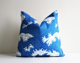 Puede incluir: Almohada azul y blanca con un patrón de olas. Las olas están delineadas en blanco y el fondo es azul sólido.