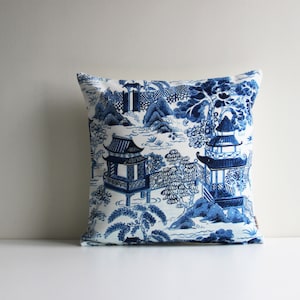 May include: Blue and white throw pillow with a traditional Chinese garden design. The pillow features a white background with blue pagoda buildings, trees, and water.