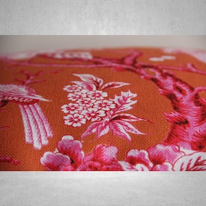 May include: Orange fabric with a pink and white floral pattern. The pattern features birds, flowers, and branches.
