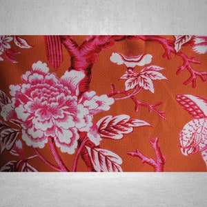 May include: Orange fabric with a pink and white floral pattern. The pattern features large flowers with pink petals and white centers, along with smaller flowers and leaves.