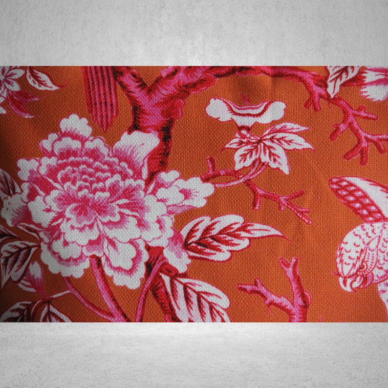 May include: Orange fabric with a pink and white floral pattern. The pattern features large flowers with pink petals and white centers, along with smaller flowers and leaves.