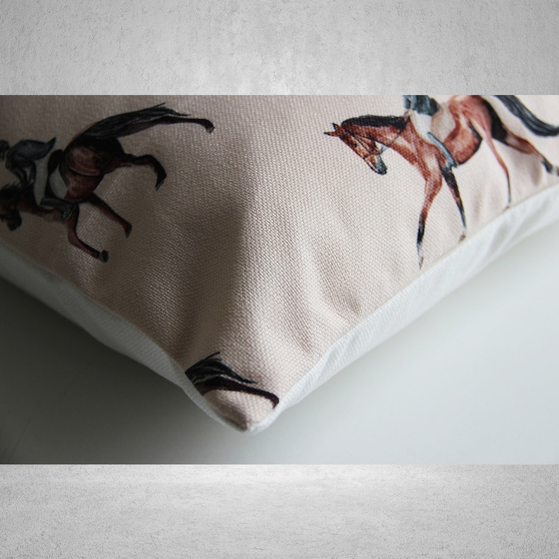 May include: A beige cushion with a white border features a repeating pattern of brown horses with riders. The horses are depicted in a watercolour style.