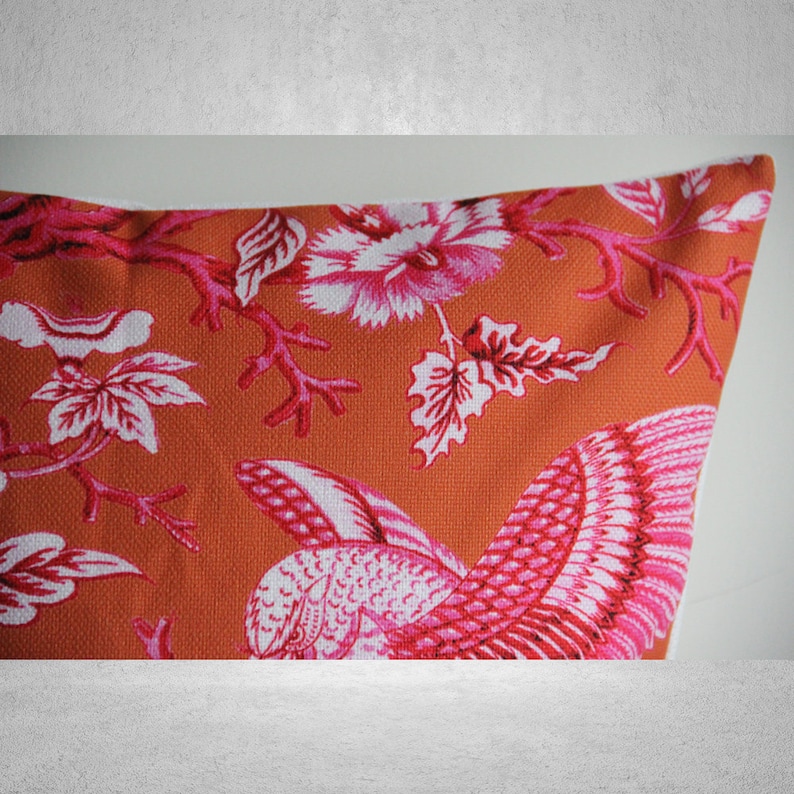 May include: Orange throw pillow with a pink and white floral pattern featuring birds and branches.