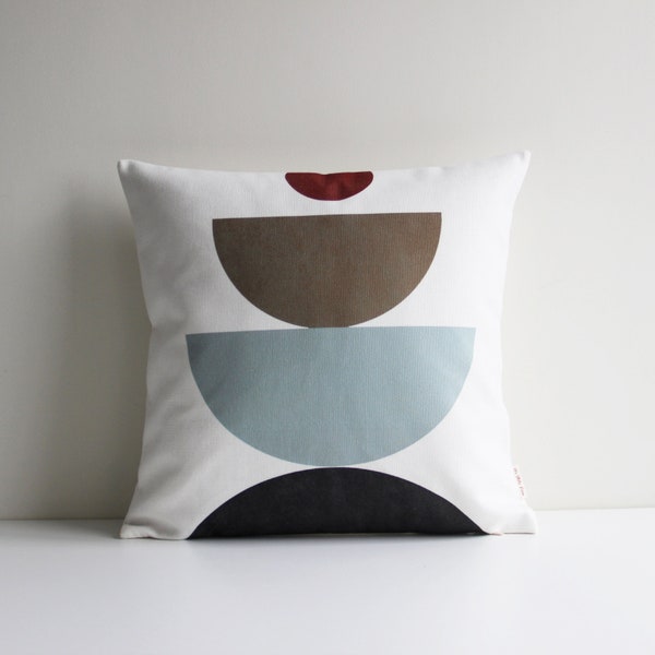 Puede incluir: Una almohada blanca con un diseño geométrico que presenta un patrón de semicírculos negros, azules, marrones y rojos.