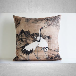 May include: A decorative throw pillow with a beige background featuring a black and white illustration of two cranes in a landscape setting. The illustration is reminiscent of traditional Japanese art.