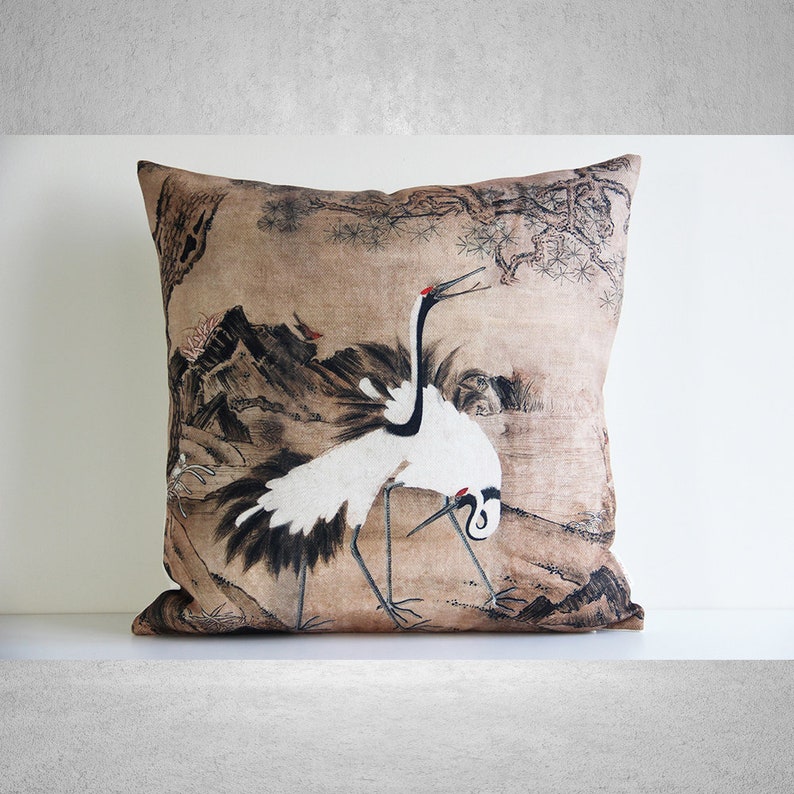 May include: A decorative throw pillow with a beige background featuring a black and white illustration of two cranes in a landscape setting. The illustration is reminiscent of traditional Japanese art.