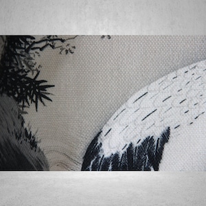 May include: A close-up of a white fabric with a black and white crane design. The fabric has a textured surface and the crane is depicted in a traditional Japanese style.