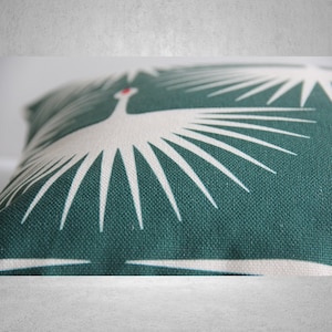May include: A green throw pillow with a white stylized bird design. The bird has a red beak and is surrounded by white rays.