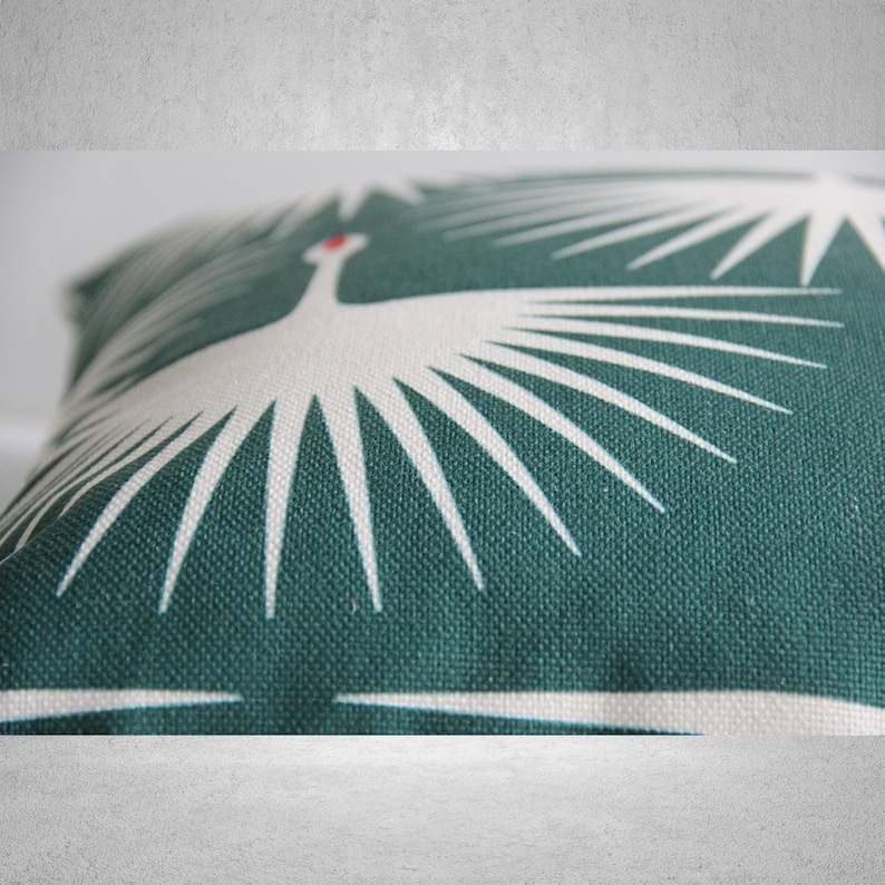 May include: A green throw pillow with a white stylized bird design. The bird has a red beak and is surrounded by white rays.