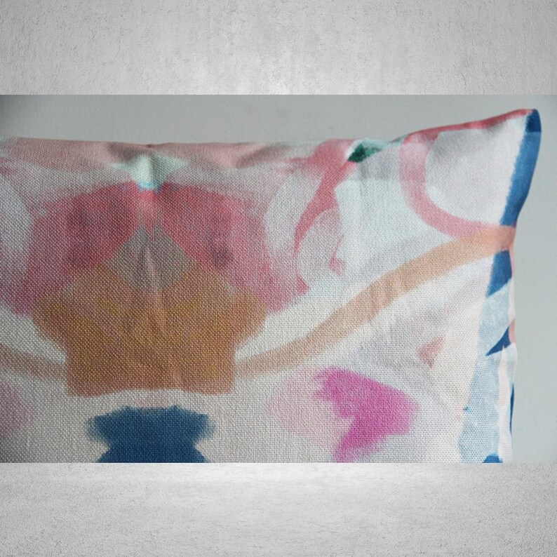 May include: A rectangular throw pillow with an abstract design featuring pink, blue, brown, and white watercolor-like shapes on a white canvas background.