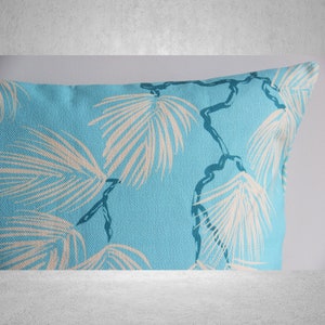May include: A rectangular turquoise pillow with a repeating pattern of off-white palm leaves and dark blue stems. The pillow has a textured appearance, suggesting a linen or similar fabric. The design evokes a tropical or coastal theme.