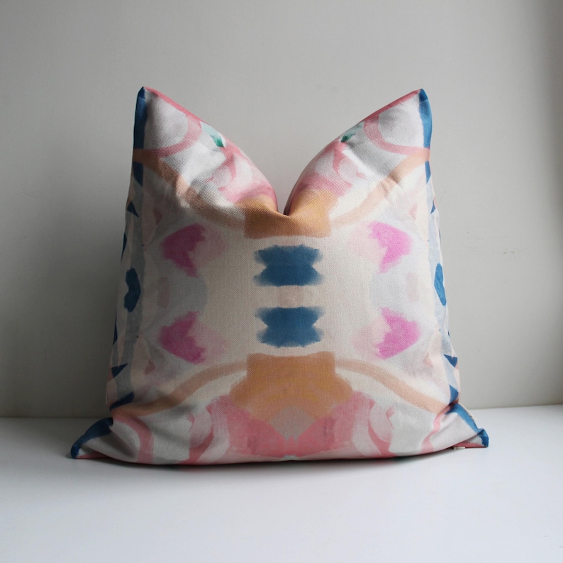 May include: A decorative pillow with a pink, orange, and blue abstract pattern. The pillow is made of a soft, textured fabric.