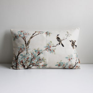 以下が含まれることがあります： 白いリネン生地の背景に、青と赤の花と枝にとまった3羽の茶色の鳥が描かれた花柄の、長方形のクッションです。