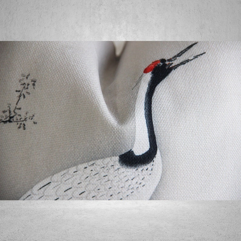 May include: A white fabric cushion with a black and white crane design. The crane has a red beak and is facing to the right. The fabric has a subtle texture.
