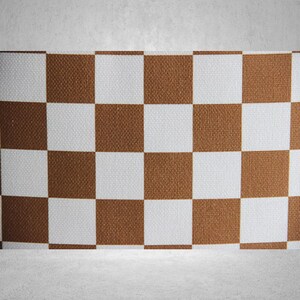 May include: A brown and white checkered pattern on a fabric surface. The fabric has a woven texture.