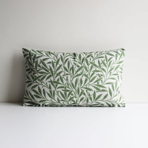 May include: A white cushion with a green leafy pattern. The cushion is rectangular and has a white background with a repeating pattern of green leaves.